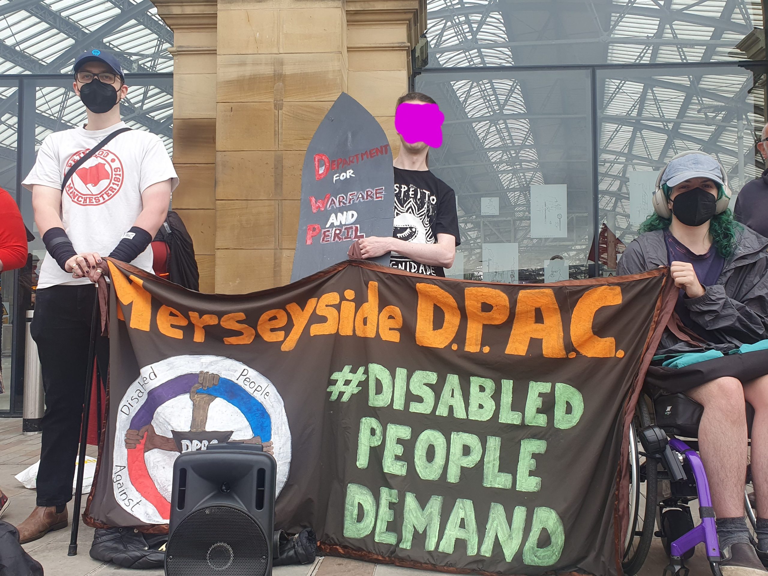 A group of protesters holding a banner reading "Merseyside DPAC #DisabledPeopleDemand"